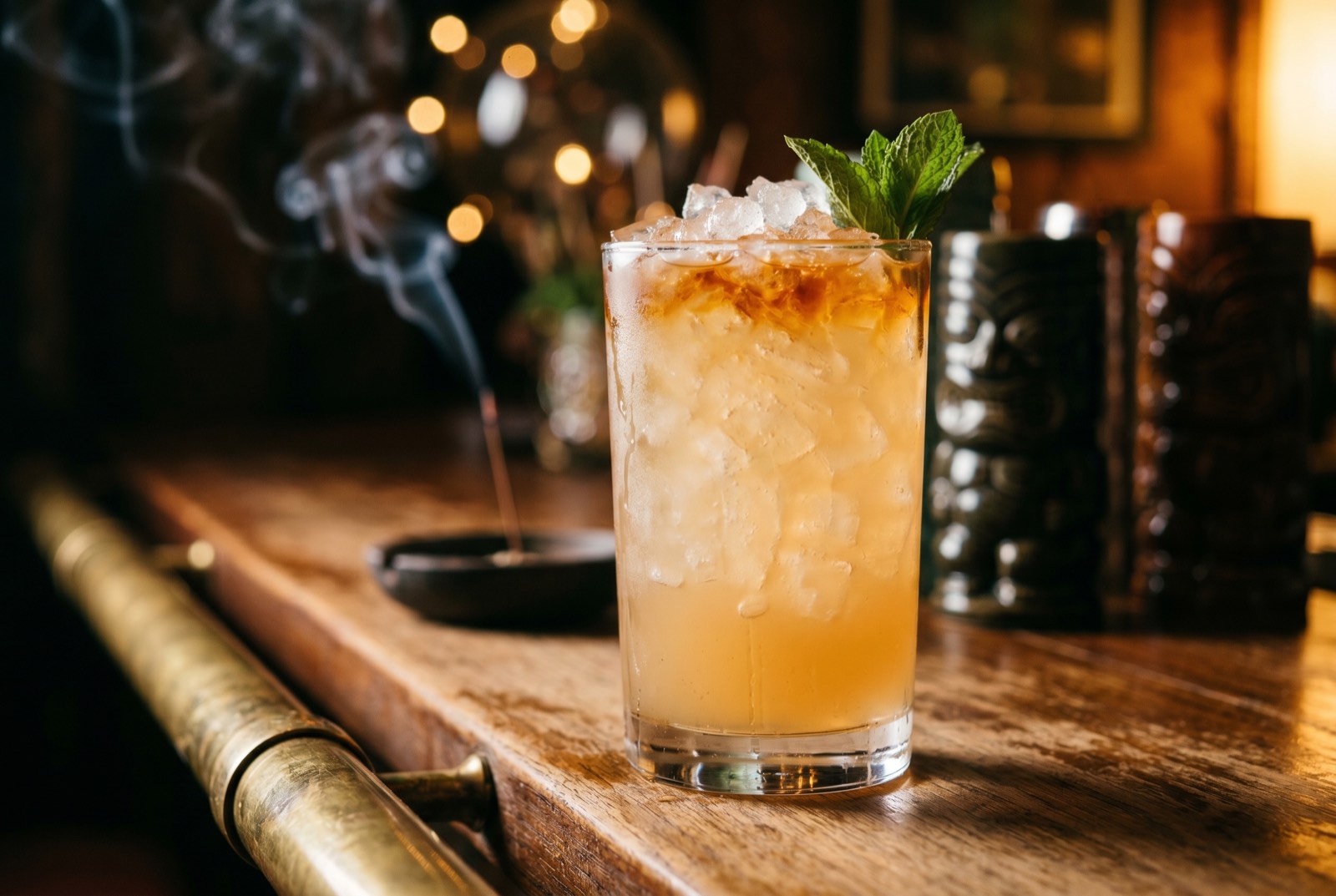 Fogcutter cocktail in a tall Collins glass over crushed ice with a sherry float and mint sprig, lit by warm tungsten light in the Forbidden Altar bar