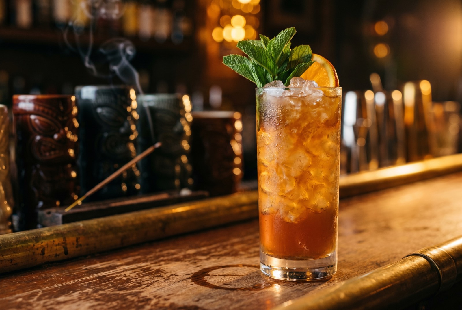 QB Cooler cocktail in a tall Collins glass over crushed ice with mint and an orange slice, lit by warm tungsten light in the Forbidden Altar bar