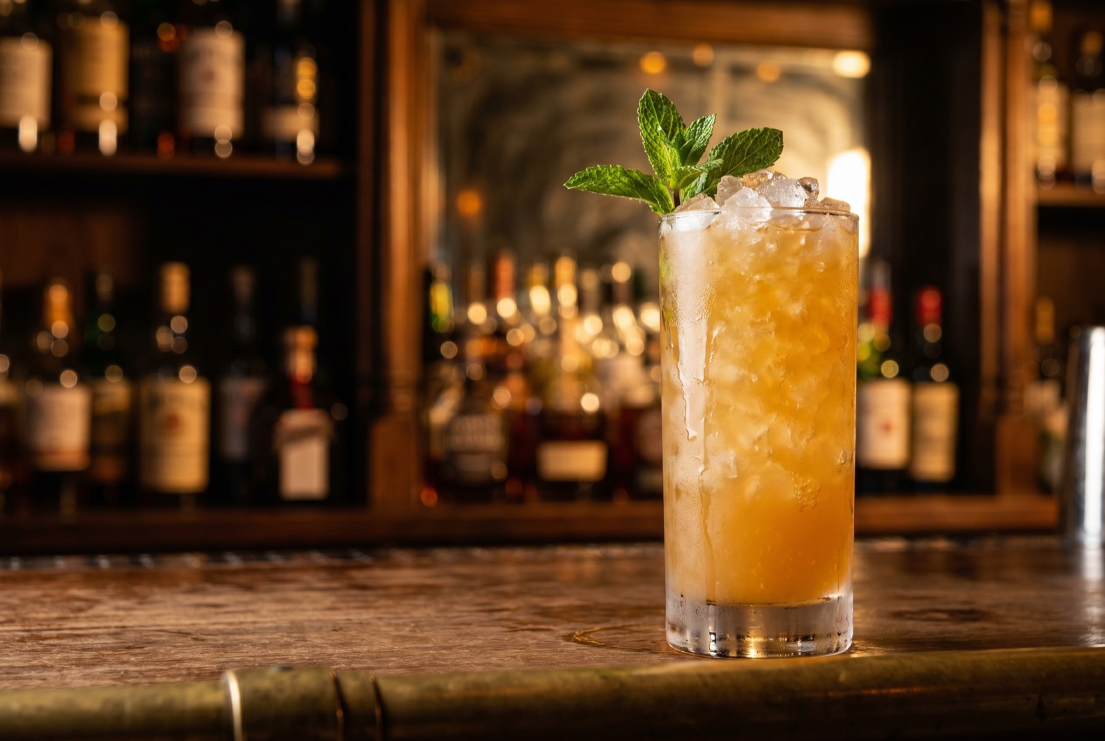 Zombie Punch in a tall zombie glass over crushed ice, bright golden-orange with a mint sprig, lit by warm tungsten light in the Forbidden Altar bar